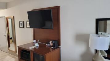 Ein Hotelzimmer mit einem Holztisch, einem flachbildfernseher an der Wand, einer Mikrowelle und einer Lampe.