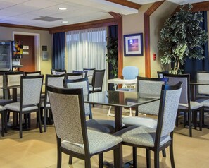 A hotel dining area with multiple tables and chairs, a vending machine, and a large potted plant.