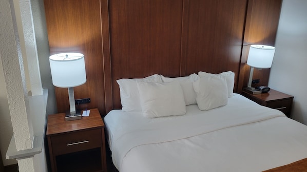 Habitación de hotel con cabecera de madera, ropa de cama blanca, dos mesitas de noche con lámparas y un pequeño cajón.