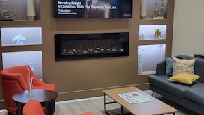 A modern living room with a flat-screen TV, red armchairs, a coffee table, and decorative shelves.