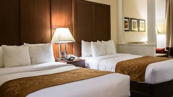 A hotel room with two beds, a nightstand with a lamp, and a view of the hallway.