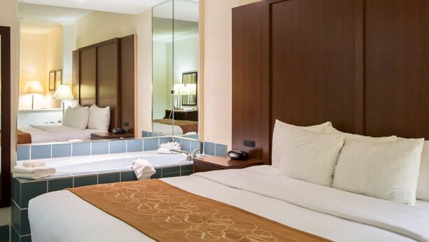 A hotel room with a large bed, a bathroom with a bathtub, and a mirror reflecting the room.