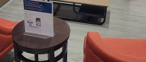A modern lobby with a grey sofa, orange armchairs, a coffee table, and a desk with a computer.