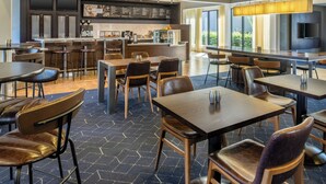 Un restaurante moderno con una zona de bar, diversas opciones de asientos y un amplio ventanal que proporciona luz natural.