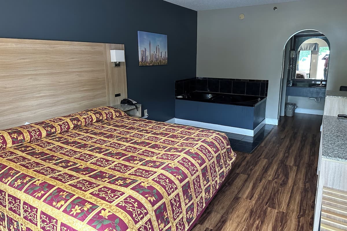 A hotel room with a large bed, a built-in bathtub, and a small bathroom.