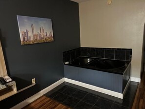 A bathroom with a black bathtub, a cityscape painting on the wall, and a wooden telephone stand. - Jameson Inn Conyers (Conyers)