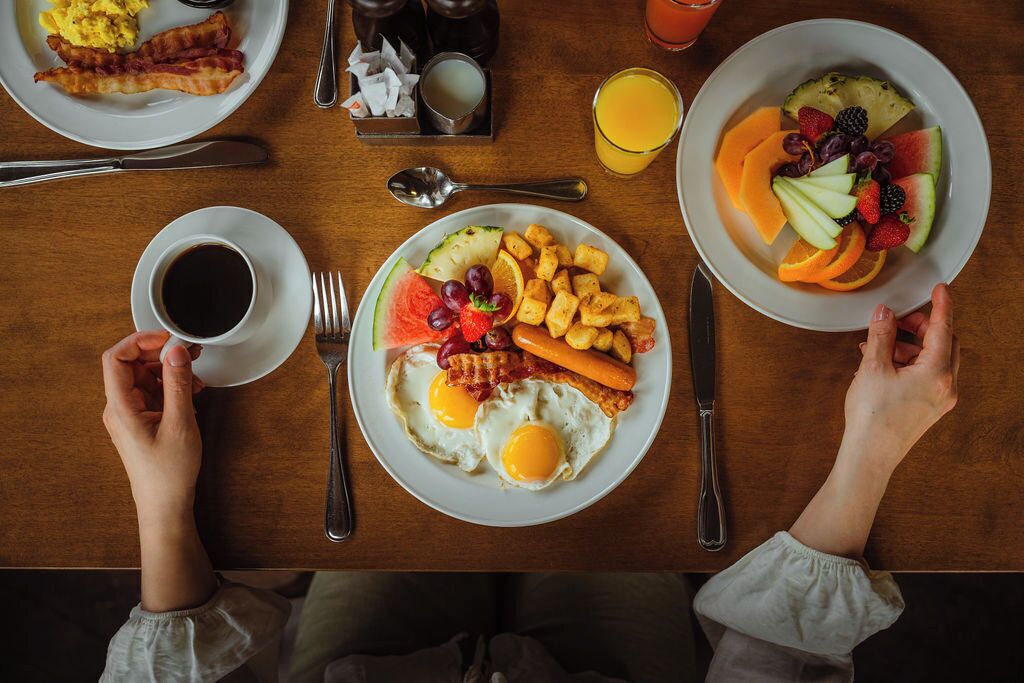 Ein Frühstückstisch mit Eiern, Speck, Toast und Obst.