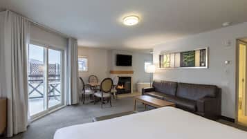 Habitación de hotel con una cama grande, un sofá, una mesa de comedor con sillas, una chimenea y un balcón con vistas al exterior.