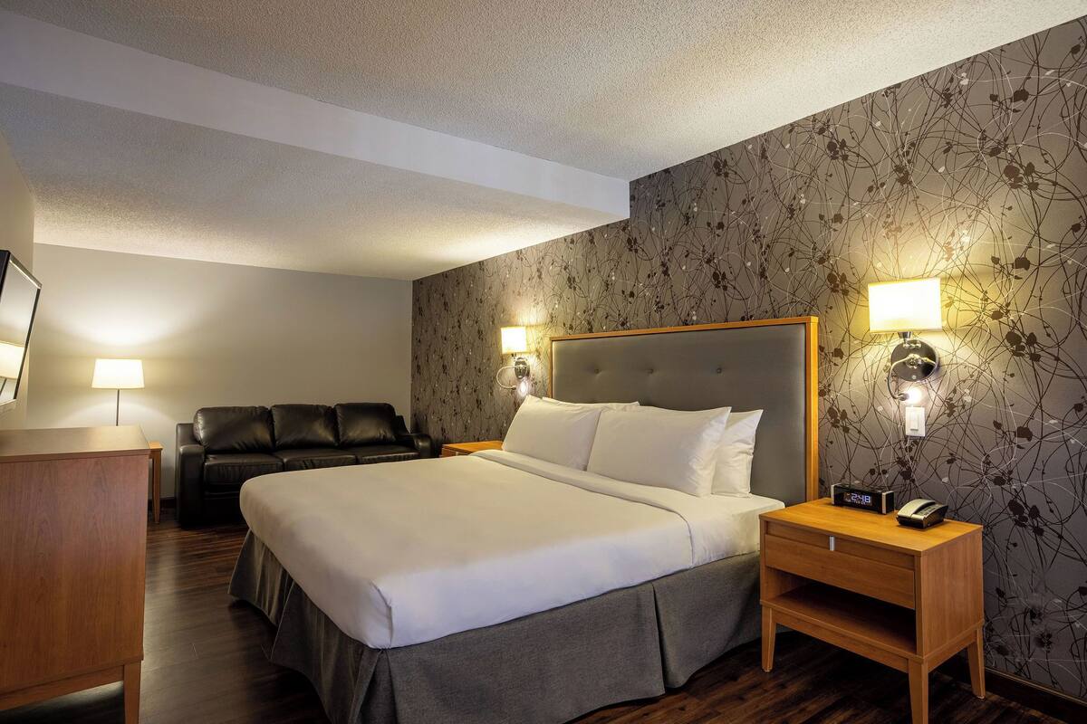 A hotel room with a large bed, two bedside lamps, a wooden nightstand, a desk, and a leather chair.