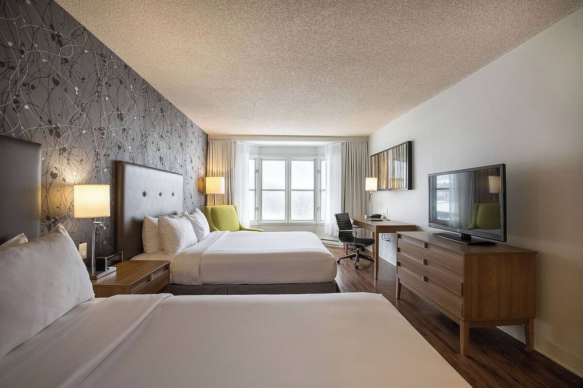 A hotel room with two beds, a desk with a computer, a TV, and a large window.