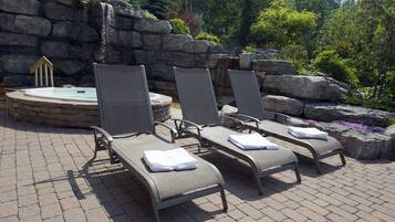 Three lounge chairs with towels, a hot tub, and a waterfall backdrop.