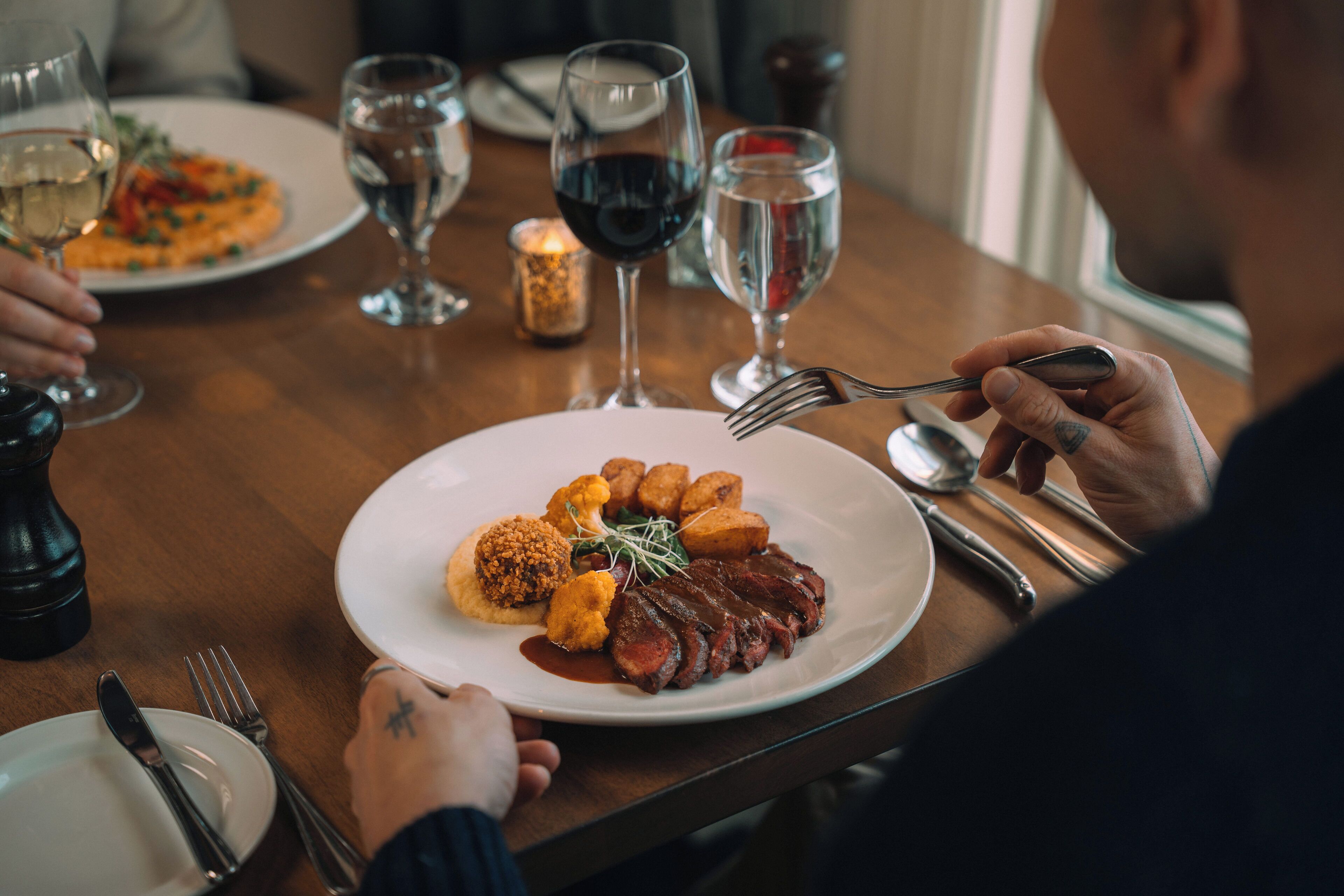 A dining table with plates of food, wine glasses, and cutlery.