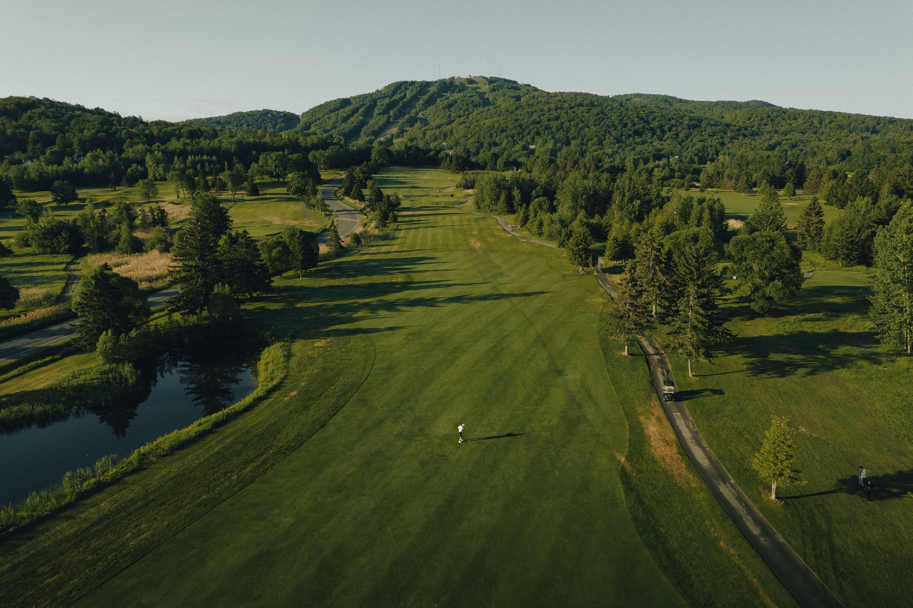 An aerial view of a golf course with a pond, trees, and a hilly landscape.