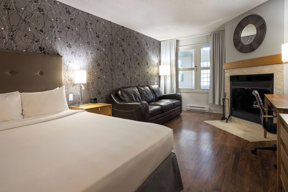 A hotel room with a large bed, a leather sofa, a fireplace, and a view of the city.