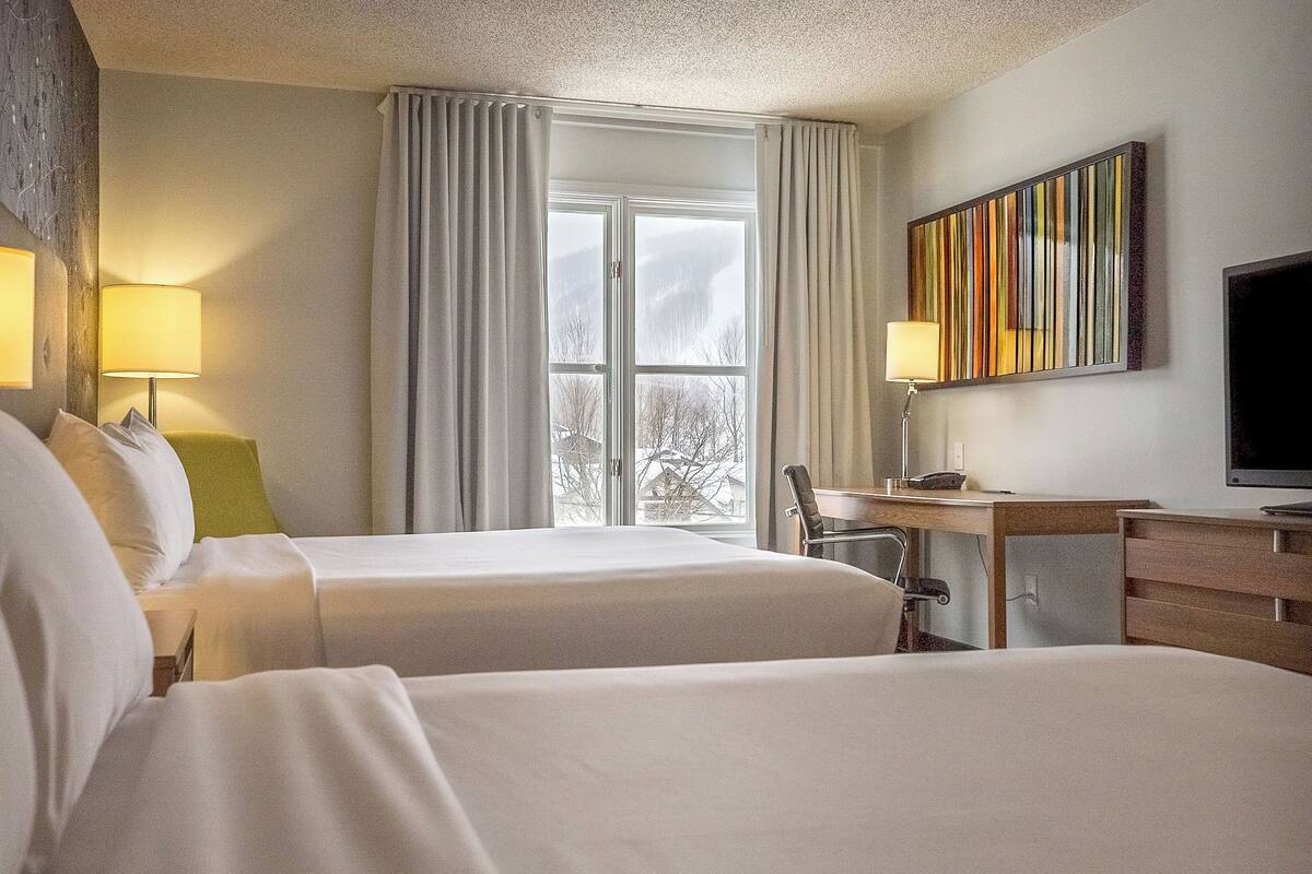 A hotel room with two beds, a desk, a chair, a television, and a window with curtains.