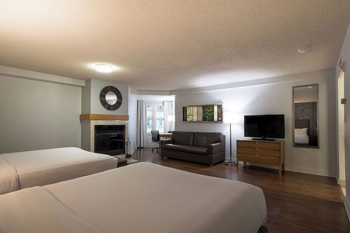 A hotel room with two beds, a sofa, a TV, and a fireplace.