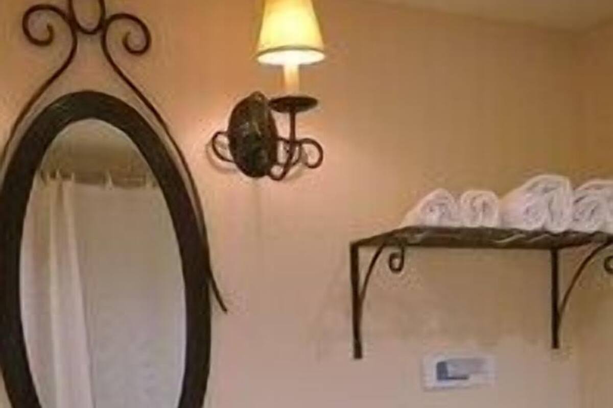 A bathroom with a sink, mirror, wall-mounted light, and a toilet.