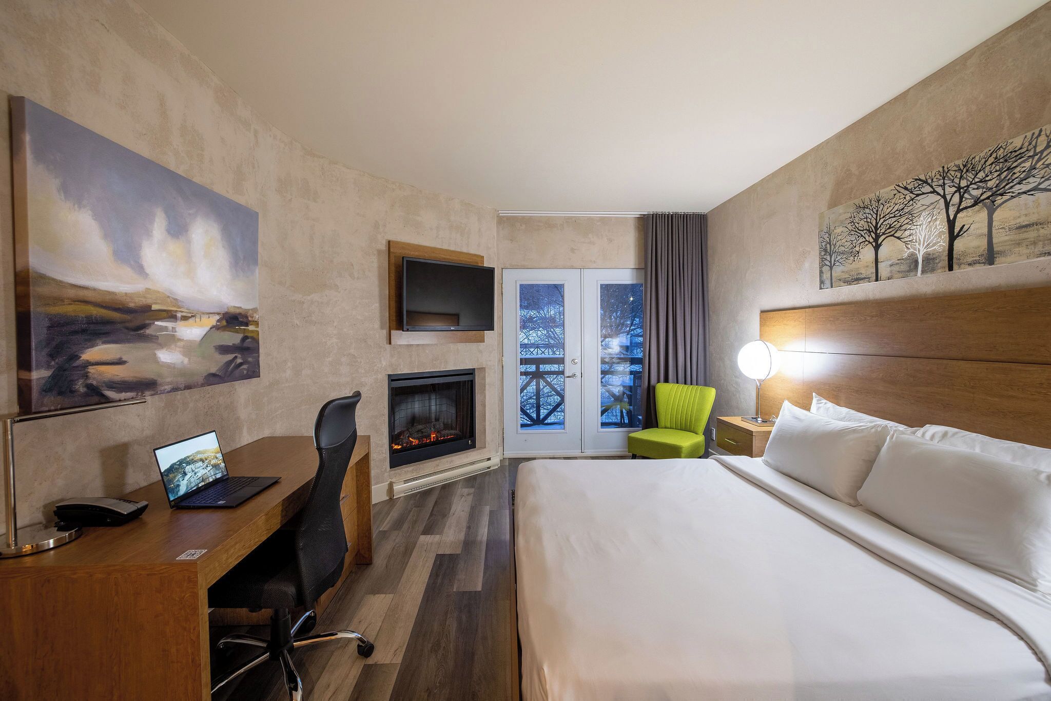 Une chambre d’hôtel équipée d’un lit, d’un bureau, d’un ordinateur portable, d’une chaise, d’une cheminée, d’une télévision et d’un tableau au mur.