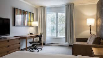 Ein Hotelzimmer mit einem Bett, einem Schreibtisch mit Stuhl, einem Fernseher, einem Fenster mit Vorhängen und einer Lampe.