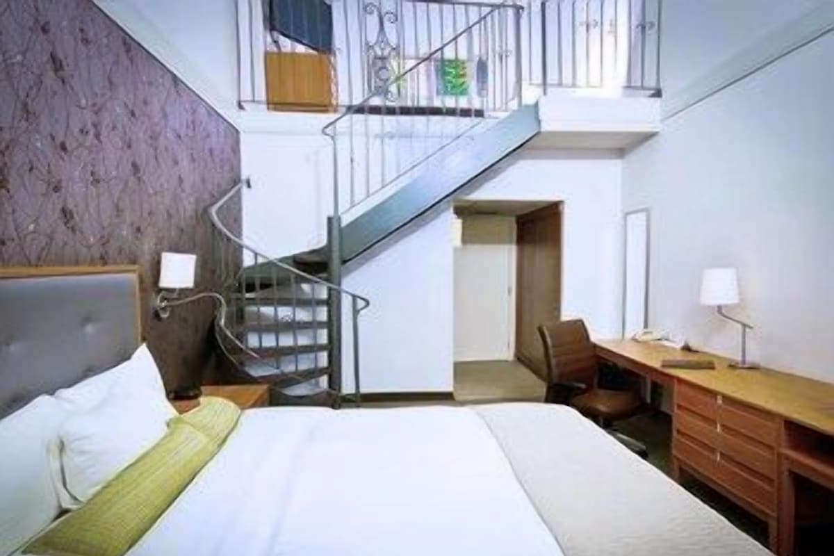 Un dormitorio con cama, escritorio, silla, escalera y vistas al exterior.