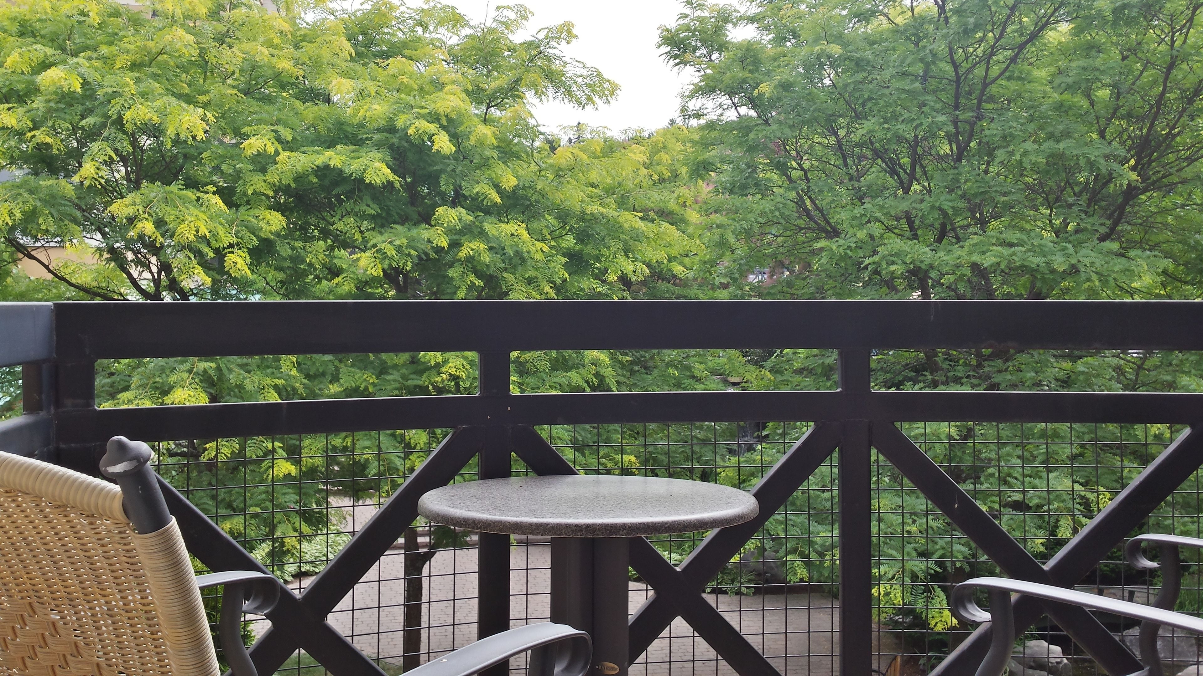 A balcony with a wicker chair, a small round table, and a metal railing.