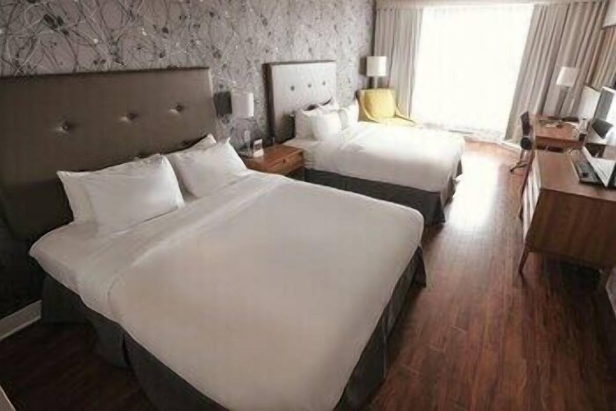 A hotel room with two beds, a wooden floor, a marble wall, and a desk with a lamp.