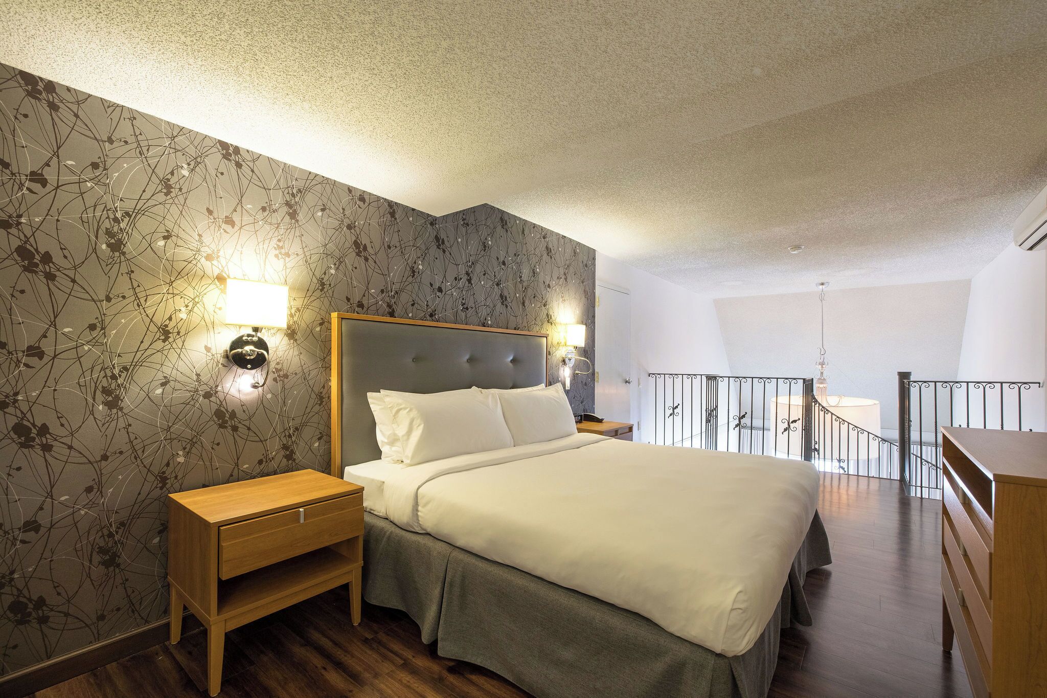 Une chambre à coucher avec un grand lit, une table de chevet, une commode et un balcon doté d’une balustrade.
