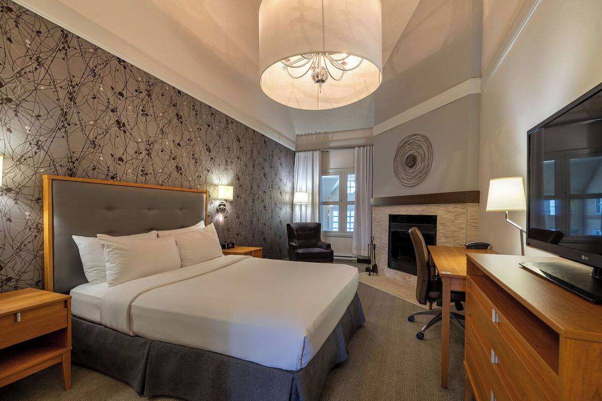 A hotel room with a large bed, a television, a desk, and a fireplace.