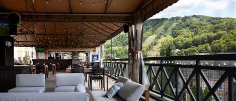 An outdoor seating area with cushioned benches and tables, overlooking a lush green hillside.