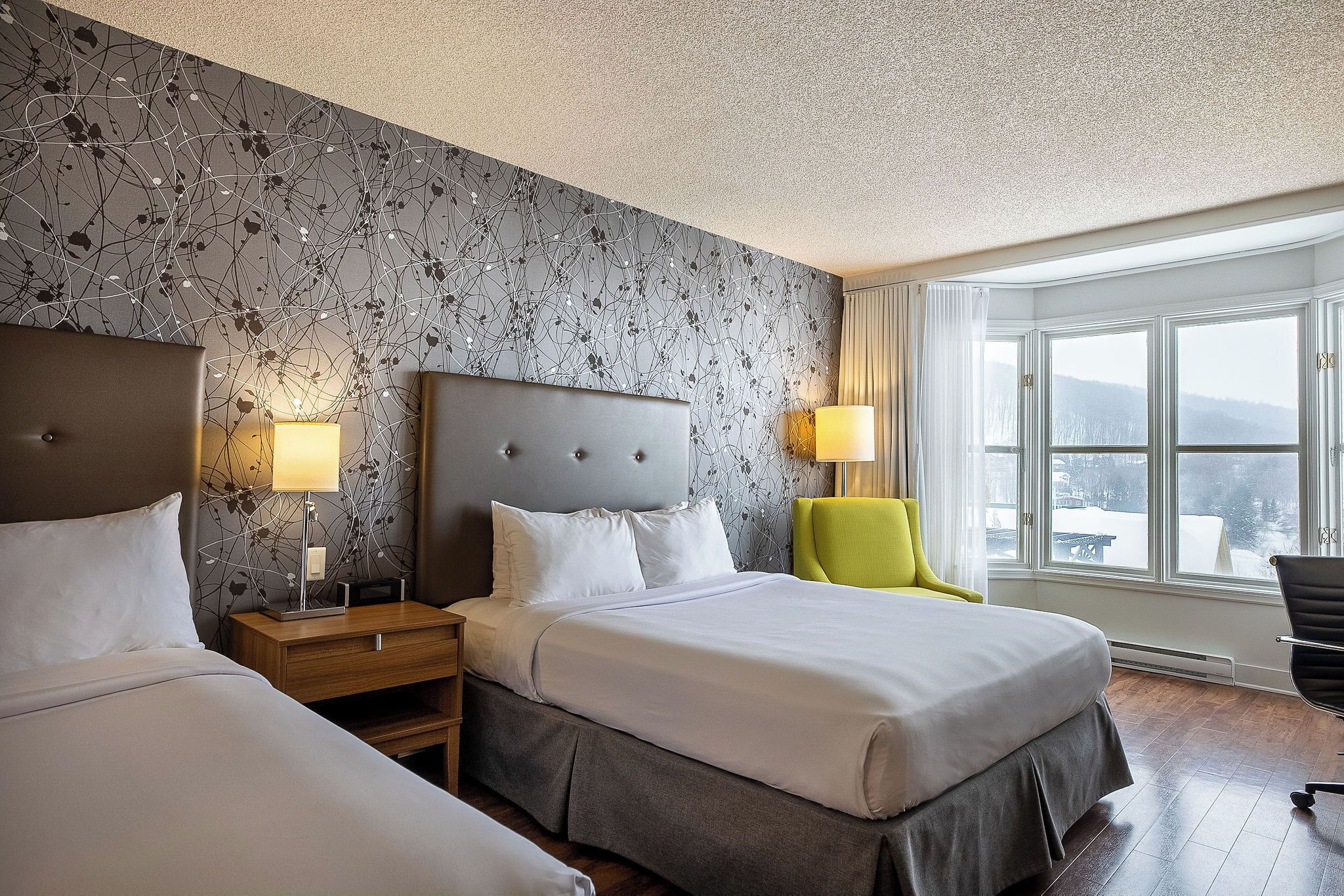 A hotel room with two beds, a large window with a view, and a modern wall design.