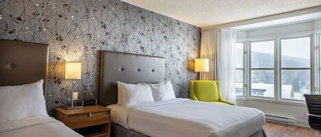 A hotel room with two beds, a large window with a view, and a modern wall design.