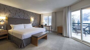 A hotel room with a large bed, a desk, a chair, and a balcony with outdoor furniture.