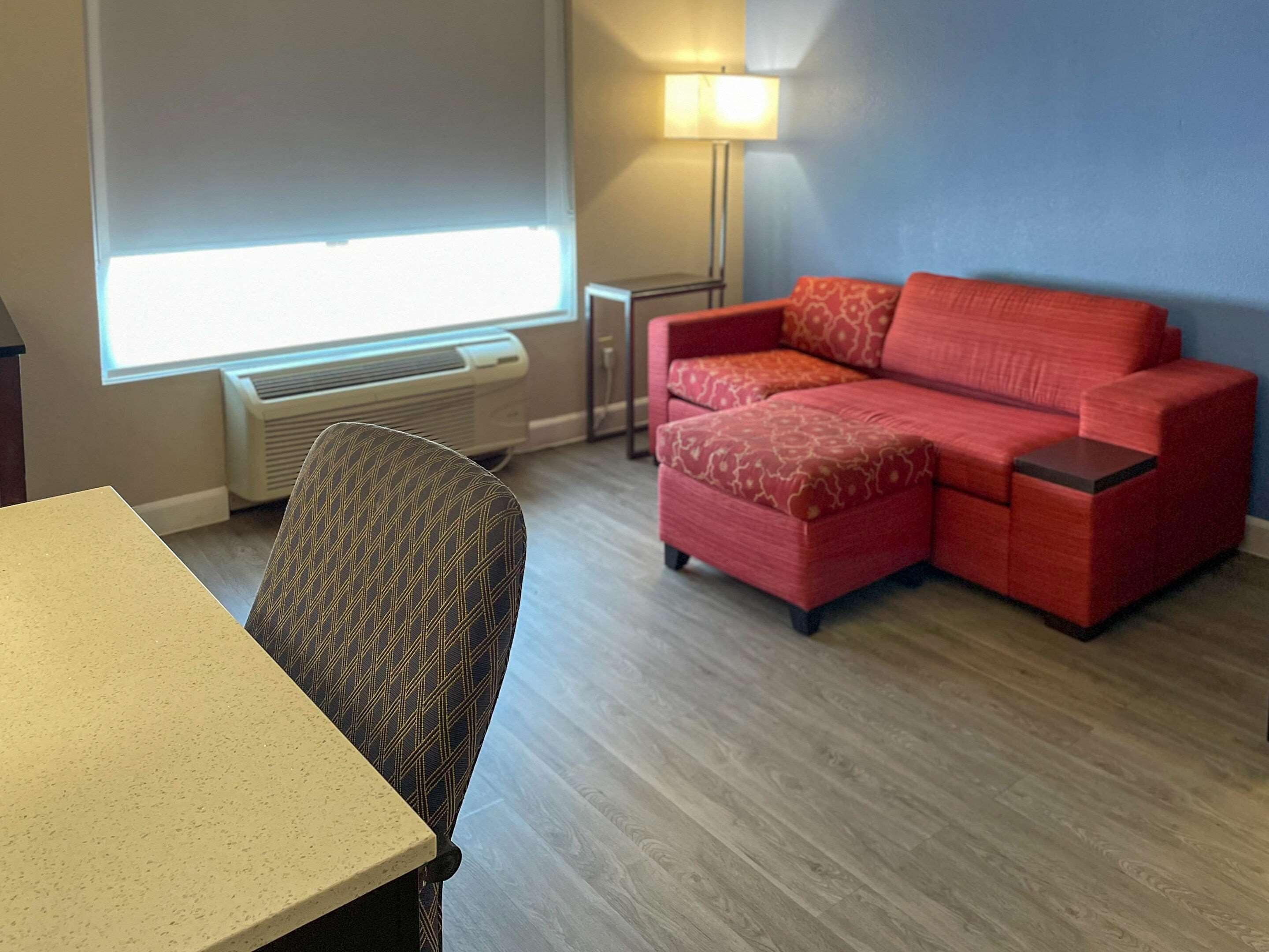 Ein Zimmer mit einem roten Sofa, einem gemusterten Sessel, einem kleinen Tisch und einer Lampe.