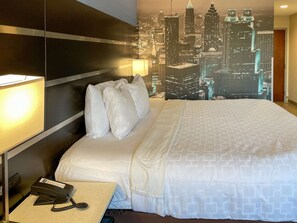 A hotel room with a bed, pillows, a nightstand with a telephone, and a cityscape mural on the wall.