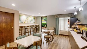 A dining area with a buffet setup, including a refrigerator, a sink, and a window with curtains.