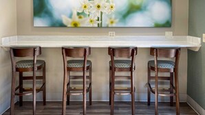 A bar area with a long counter and three wooden chairs with patterned cushions.