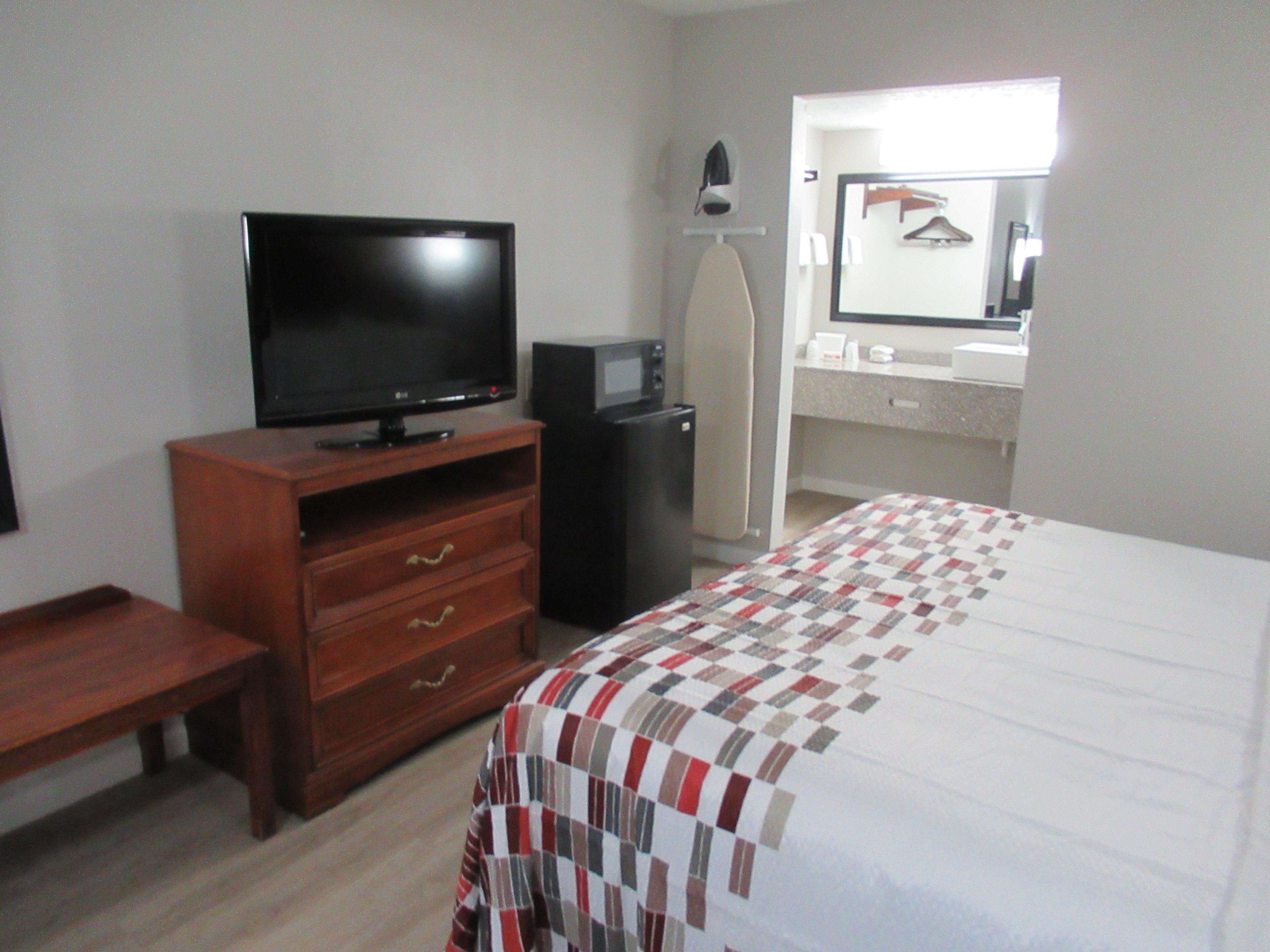 A hotel room with a television, a refrigerator, a bed with a quilt, a dresser, and a mirror.