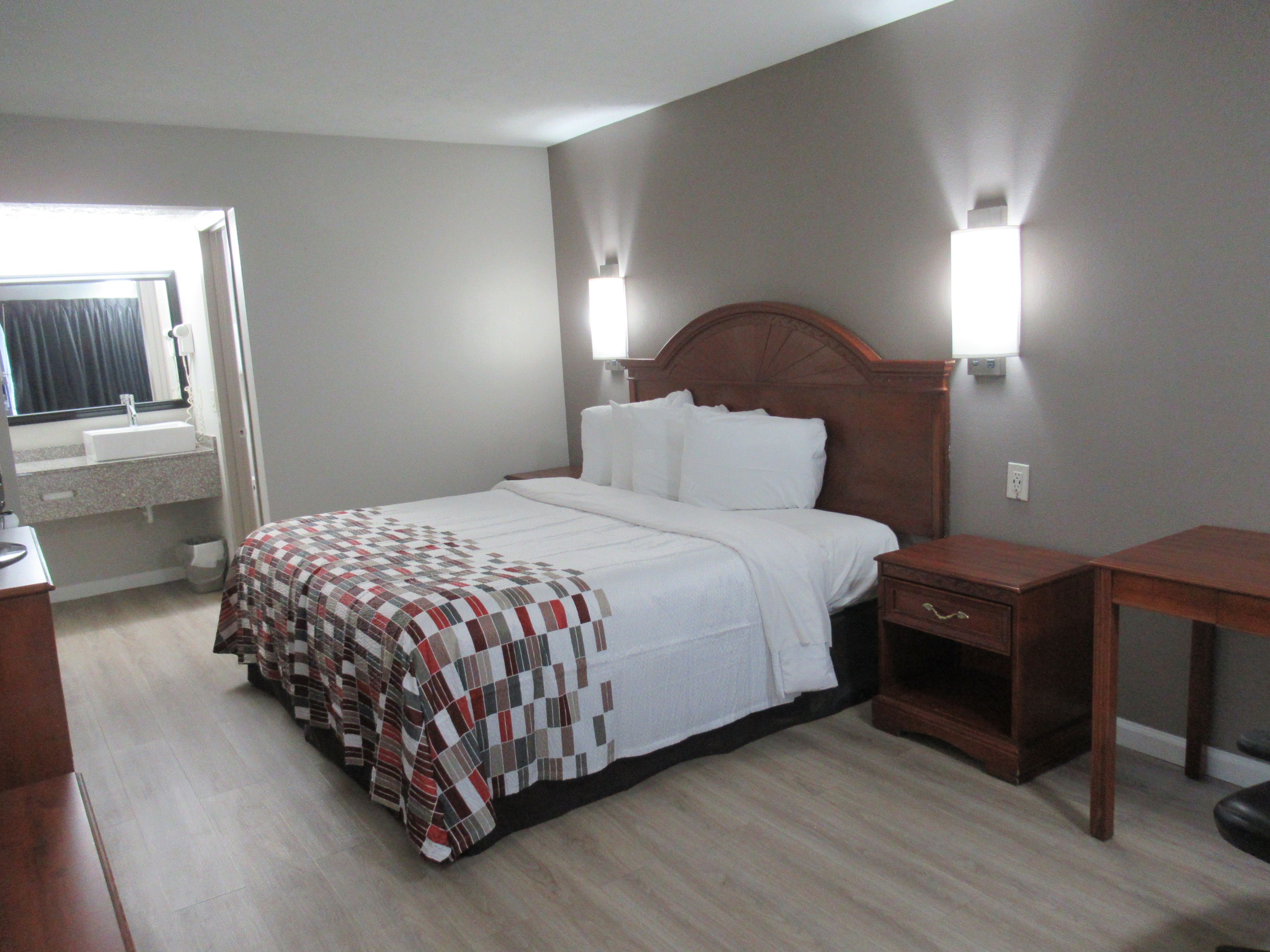 A hotel room with a bed, bedside table, and a window with curtains.