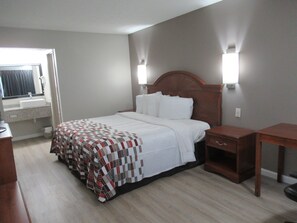 Una habitación de hotel con cama, mesita de noche y ventana con cortinas.