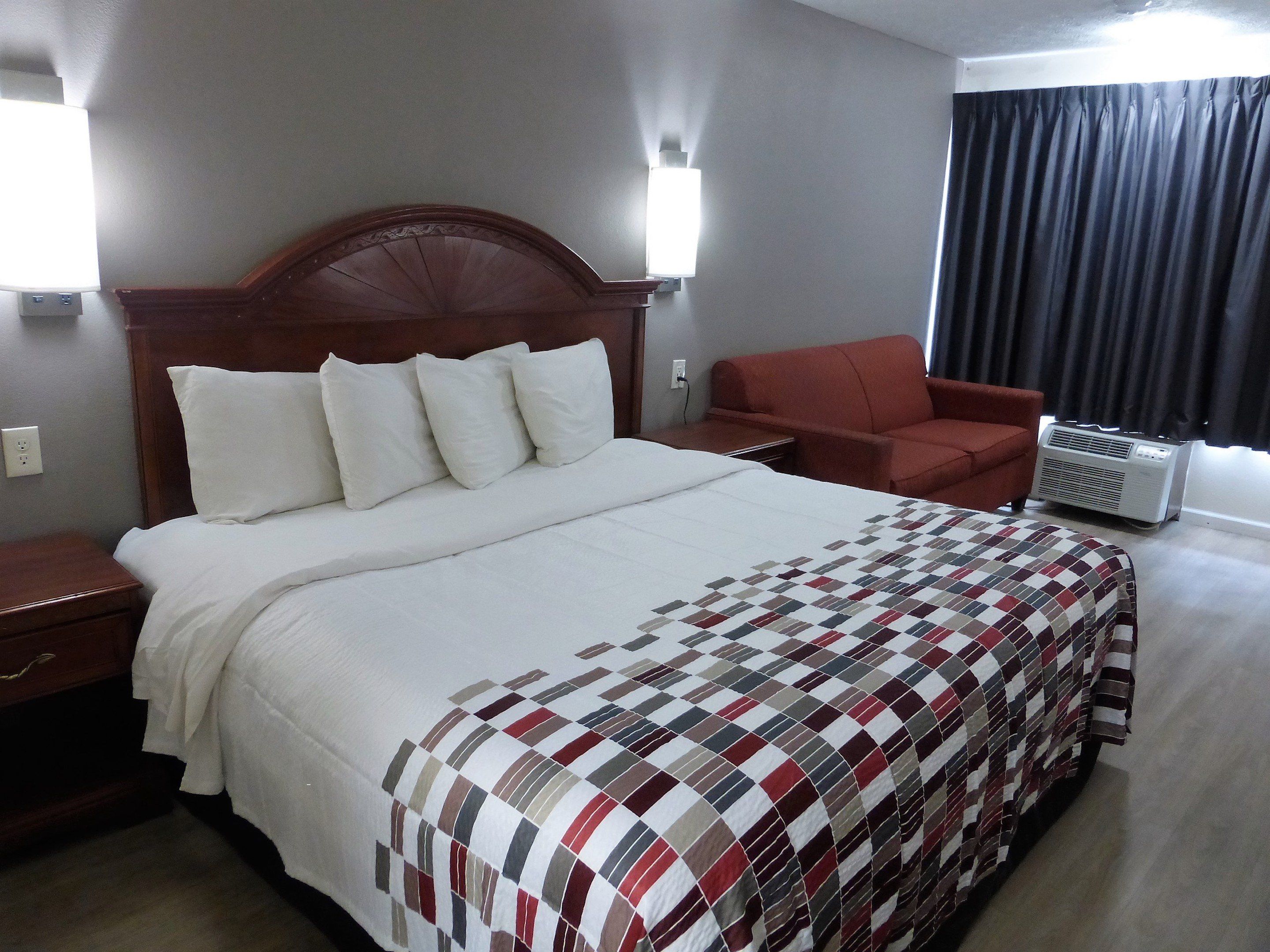 Habitación de hotel con una cama grande, un sillón rojo, un calefactor portátil y una lámpara de pared.