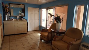 A room with a kitchenette, a dining area with a table and chairs, a large mirror, and a view through a window.