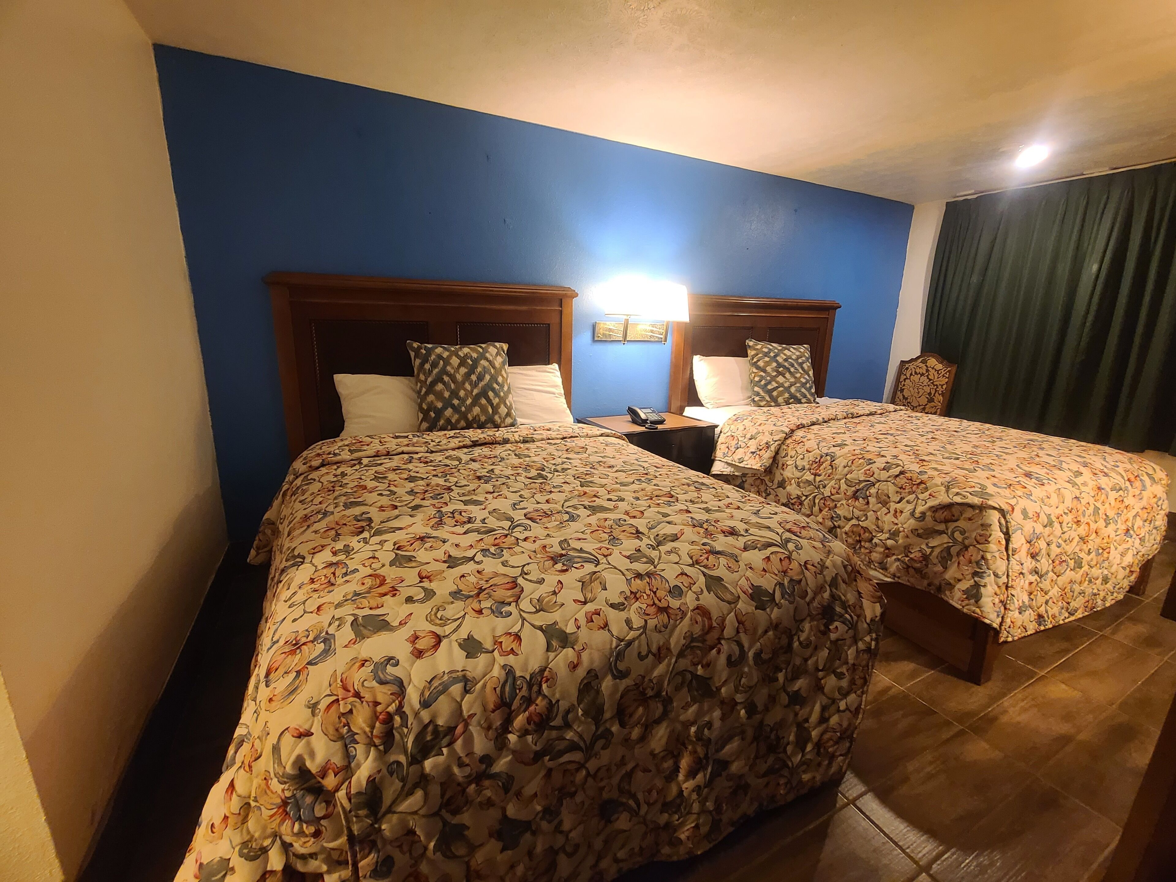 A hotel room with two beds, each with floral-patterned bedding, wooden headboards, and bedside lamps.