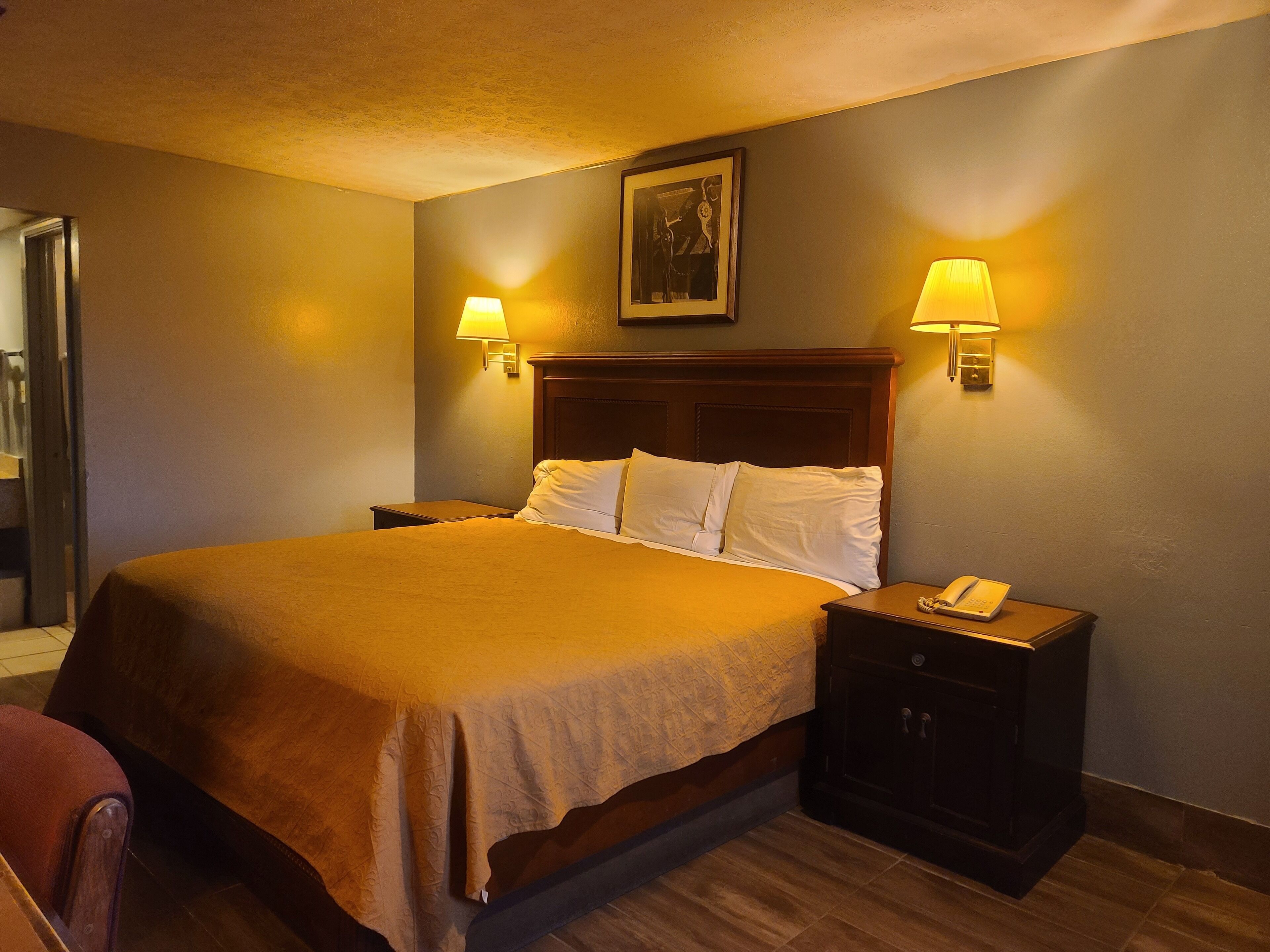 A hotel room with a large bed, two bedside lamps, a nightstand with a phone, and a framed picture on the wall.