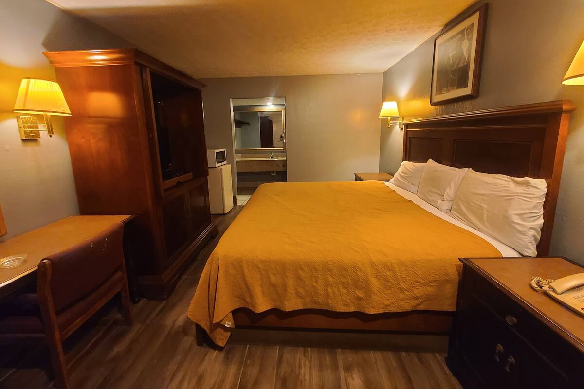 Una habitación de hotel con cama, mesitas de noche, escritorio, espejo y puerta que da a un baño.