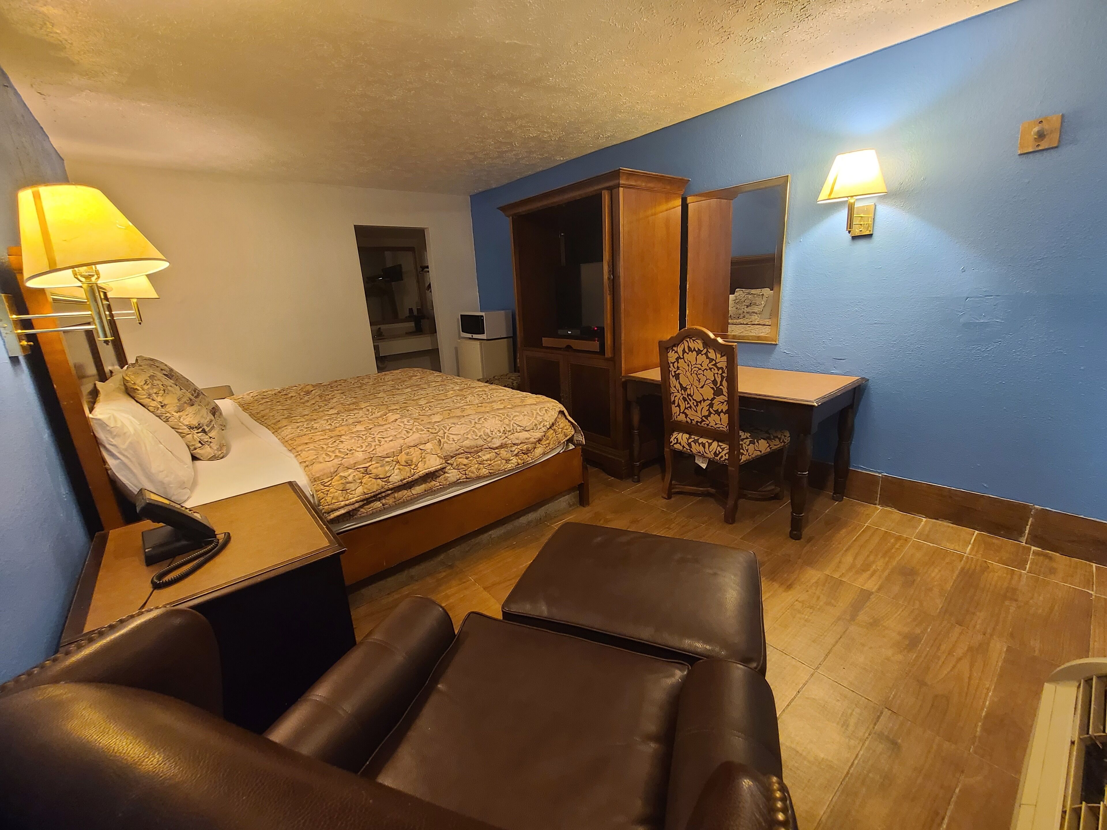 Una habitación de hotel con cama, escritorio, silla, lámpara y armario.