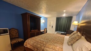A hotel room with a bed, a desk with a microwave, a chair, and a television.