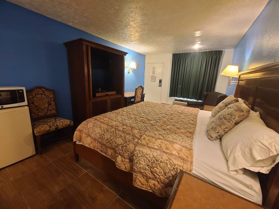 A hotel room with a bed, a desk with a microwave, a chair, and a television.