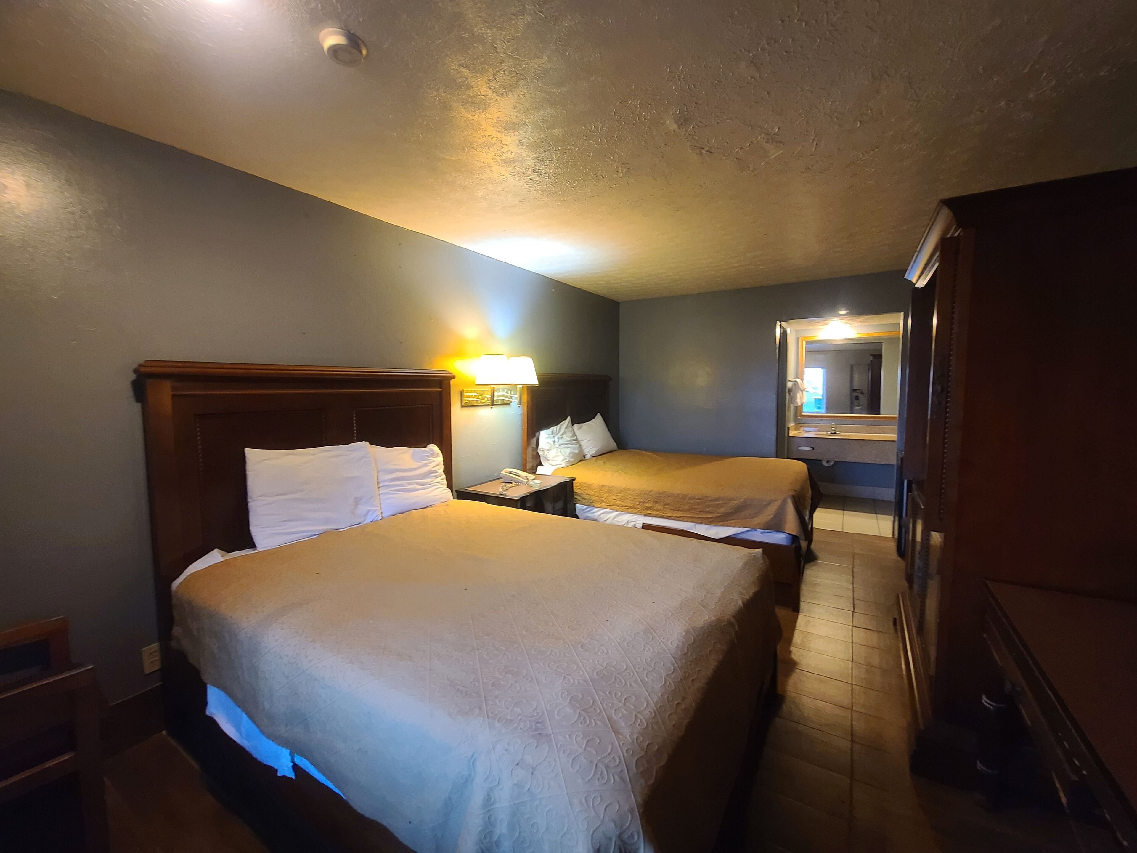 A hotel room with two beds, a nightstand with a lamp, a mirror, and a wooden wardrobe.