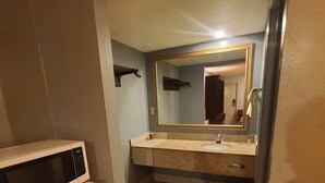 A compact bathroom with a sink, mirror, and a microwave placed on a small refrigerator.