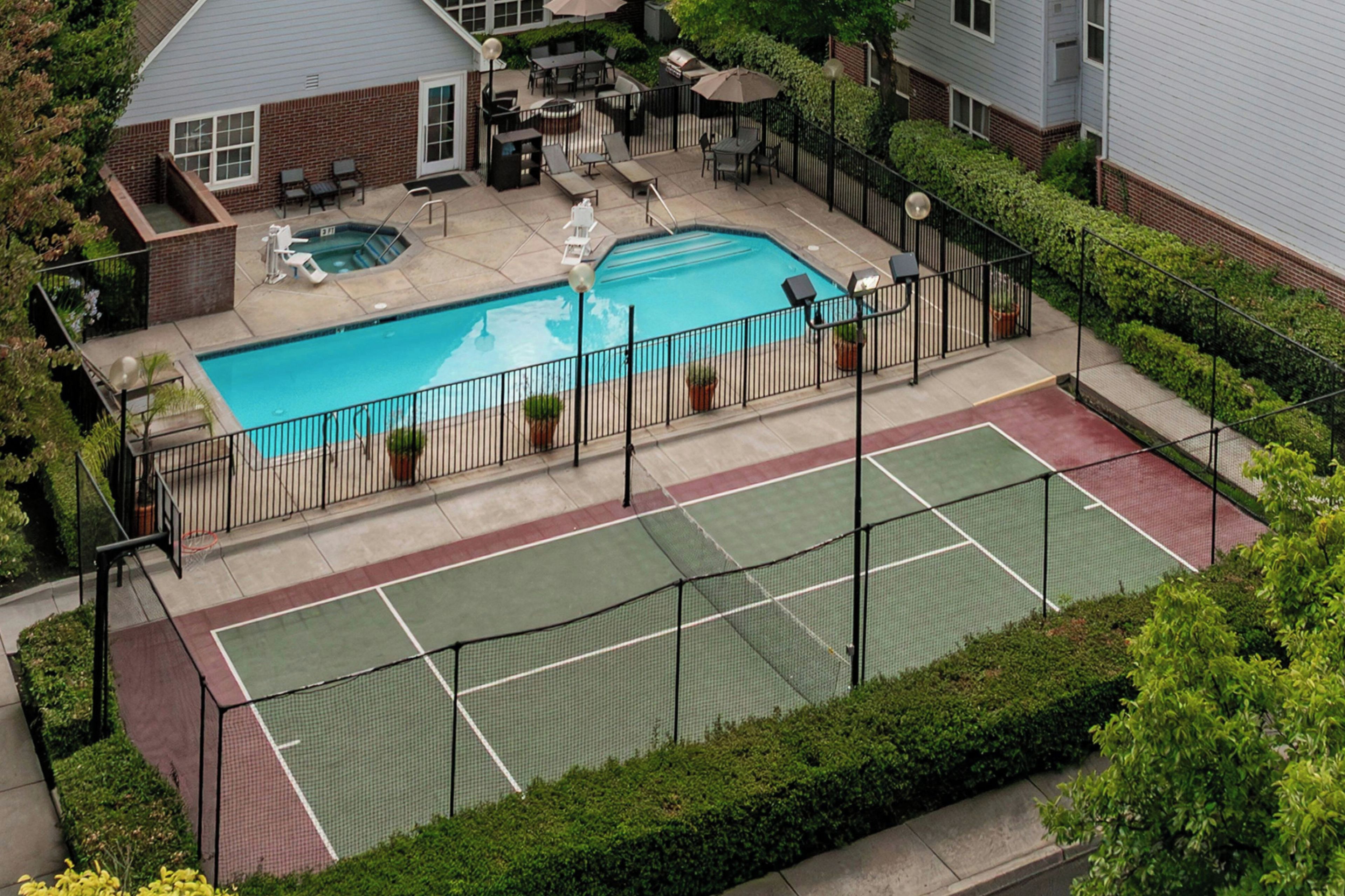Piscina residencial con cancha de tenis y mobiliario de patio.